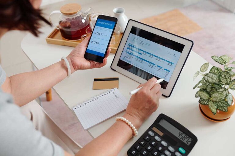 Person reviewing account alerts and a household budget on a smartphone at a kitchen table.